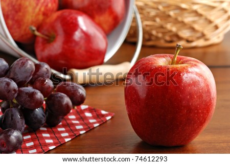 Fresh gala apple with grapes on wood table.  Additional apples spilling from bucket in background.  Macro with shallow dof.