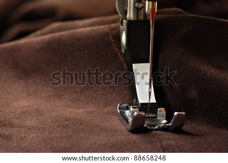 Sewing machine presser foot with threaded needle raised mid-seam on brown suede cloth.  Macro with extremely shallow dof and copy space.