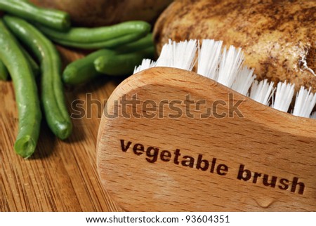Wooden vegetable brush (with words engraved) on cutting board with wet potatoes and green beans.   Macro with shallow dof.  Food safety concept.