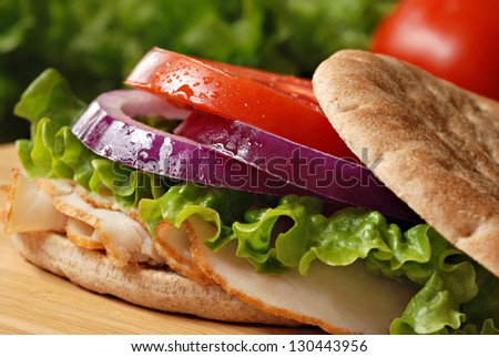Healthy turkey sandwich on thin whole wheat deli roll with lettuce, onions and tomato on wooden cutting board with tomato and lettuce in background.  Macro with shallow dof.