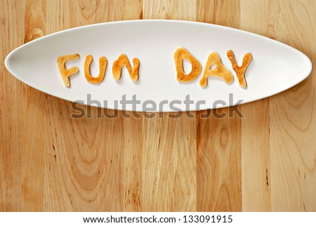 Kid\'s breakfast of mini pancakes with letters spelling out \'Fun Day\' on wood background with copy space.