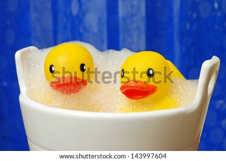 Fun still life of happy rubber duckies in bubble bath with blue shower curtain in soft focus as background.  Macro with shallow dof.
