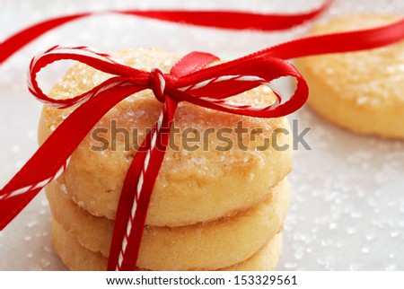 Freshly baked sugar cookies tied with festive bakers twine and red satin ribbon.  Decorating sugar crystals sprinkled in background.  Macro with shallow dof.