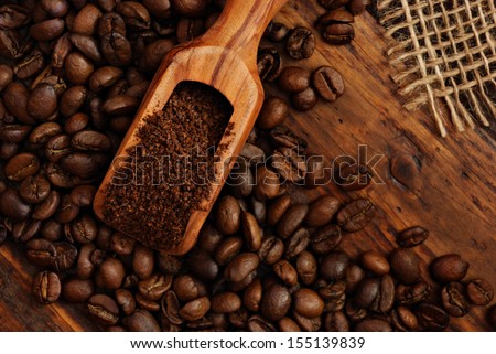 Olive wood measuring scoop with coffee beans, ground coffee and burlap on rustic dark wood background.  Low key still life with directional, natural lighting.