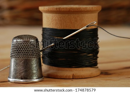 Sewing still life of antique thimble with wooden spool of thread and vintage needle on wood background.  Macro with shallow dof.  Selective focus on thimble and eye of needle.
