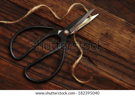 Traditional hand forged scissors with twine on rustic wood background.  Low key still life with natural, directional lighting for effect.