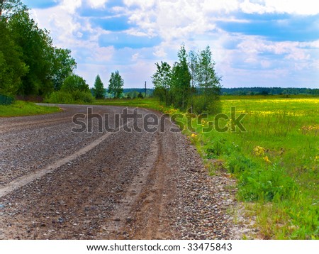 country landscape with wet gravel road through the green summer field