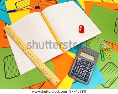 Open notebook sharpener ruler paper-clips calculator pencil and pen against the multicolored notebooks background