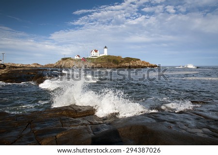 Waves crash over slippery rocks by lighthouse in Maine.