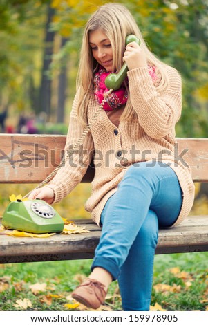 Young blond woman calling on vintage phone in autumn park
