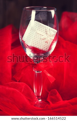 empty glass with small gift box inside and around on wooden background