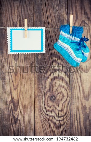 knitted baby socks and blank note hanging on clothesline against wooden background