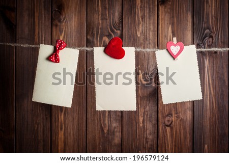 three old paper sheet with bow and hearts hanging on clothesline against wooden background
