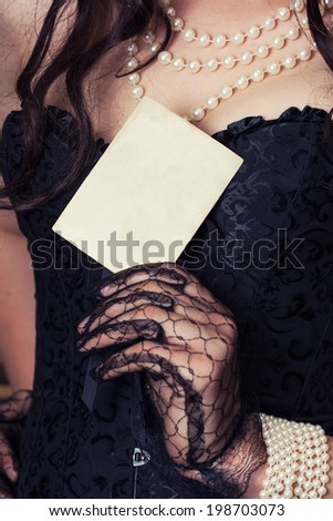 woman wearing black corset and pearls and holding a vintage paper sheet against retro background