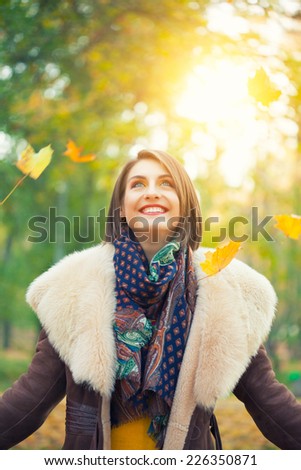 Young woman posing in autumn park with falling leaves