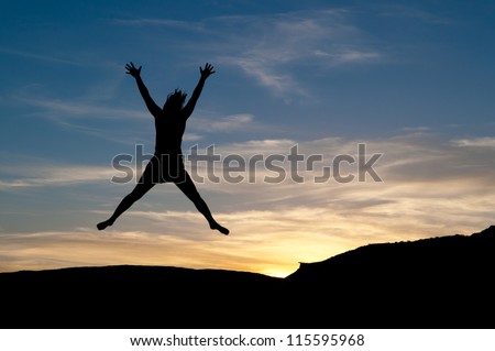 Star jump for joy at sunset. Young woman in the air as a silhouette figure.