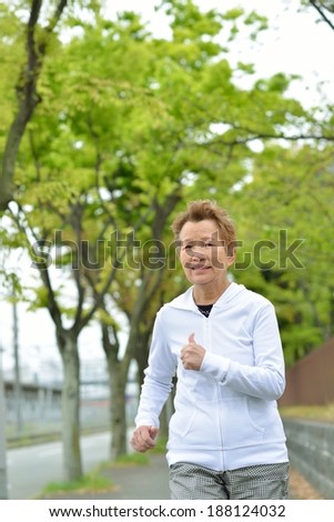 Asian elderly woman that is running the sidewalk there is a forest of the fresh green