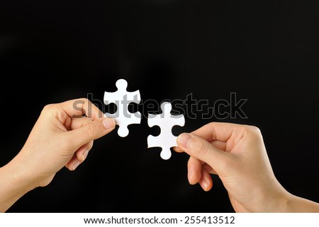 The hands of human beings that have a jigsaw puzzle that was taken with a black background