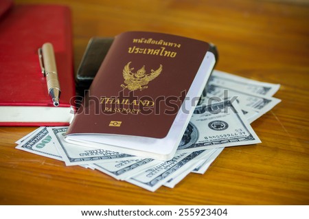 Thailand passport laying atop a pile of American dollars.Note book.
