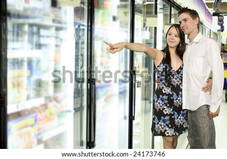 young couple looking at food near freezer in grocery store