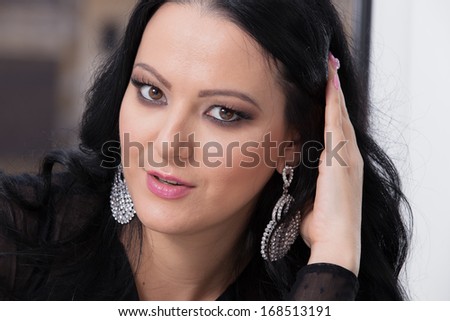 Beautiful brunette woman with jewellery  touching her long and healthy  hair. Earring. Wavy Hair.Looking at camera