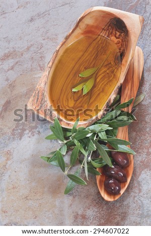 Bowl of olive oil,  olive leaves on and around a wooden spoon with black olives . Macro, selective focus, top view