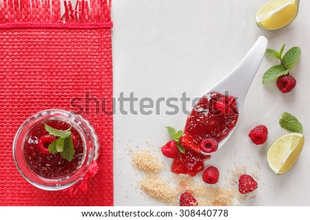 Raspberry Lemon Jam. A jar of raspberry  jam with a spoon and fresh raspberries, top view