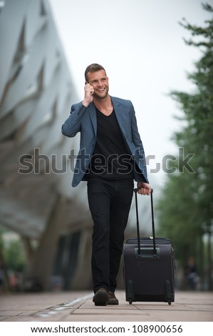Portrait of a handsome young business man walking in the city phone and suitcase