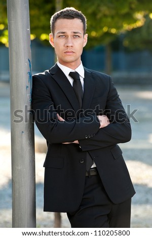 Outdoors portrait of a handsome young businessman standing alone and wearing a suit with arms crossed.