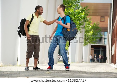 Two multicultural students walking and talking on campus. Full length portrait of an African American and Caucasian students laughing.