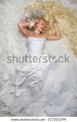 Portrait of a beautiful bride with long blond hair lying on a bed of white lace fabric