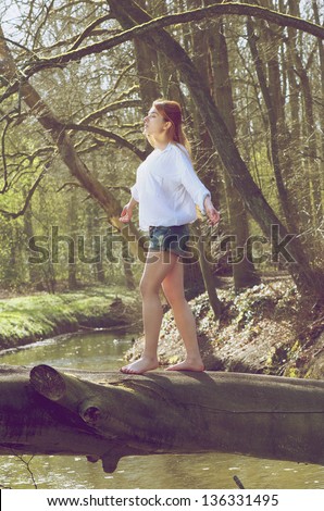 Portrait of a young woman balancing on fallen tree trunk across a stream