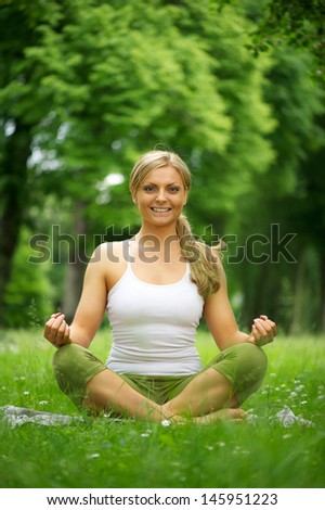 Portrait of a young woman smiling and sitting in yoga pose in the park