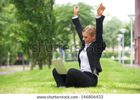 Portrait of a happy businesswoman sitting outdoors with laptop and arms up in celebration