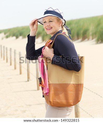 Portrait of an older woman smiling and holding her hat at the beach