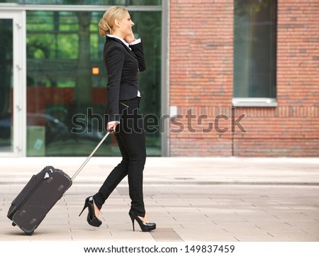 Profile portrait of a business woman walking with luggage and talking on phone