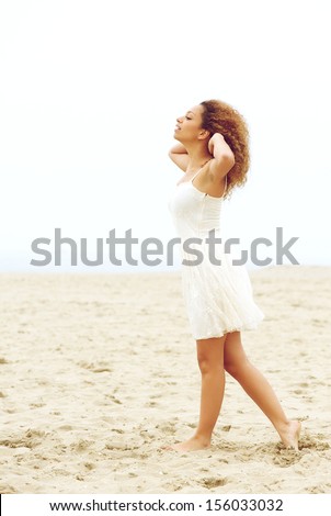 Profile portrait of a elegant young woman walking on sand with hands in hair