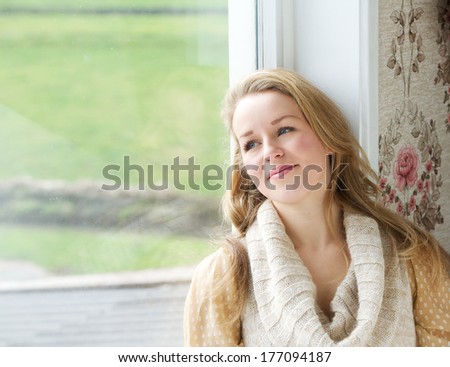 Close up portrait of a young woman sitting by window looking outside