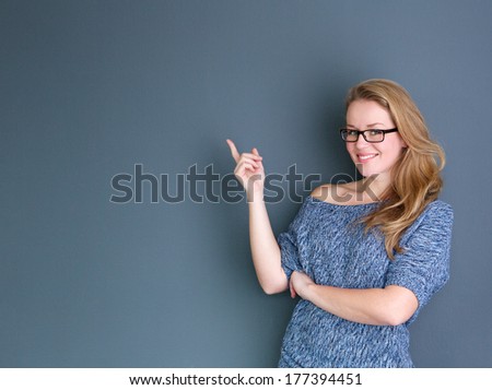 Portrait of a young woman smiling and pointing finger showing copy space against gray background