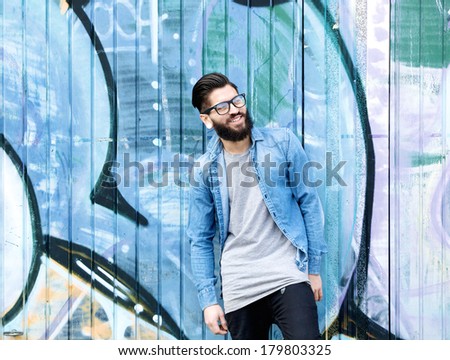 Portrait of a smiling man with beard and glasses standing against graffiti background