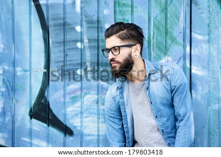 Portrait of a male fashion model with beard and glasses standing against graffiti background