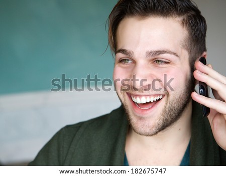 Close up portrait of a handsome young man smiling and using mobile phone indoors