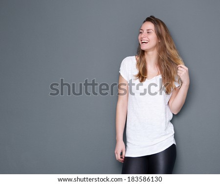 Portrait of a young woman laughing with hand in hair posing on gray background