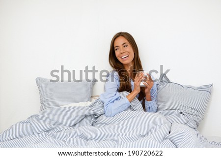 Portrait of a happy young woman smiling with cup of tea in bed