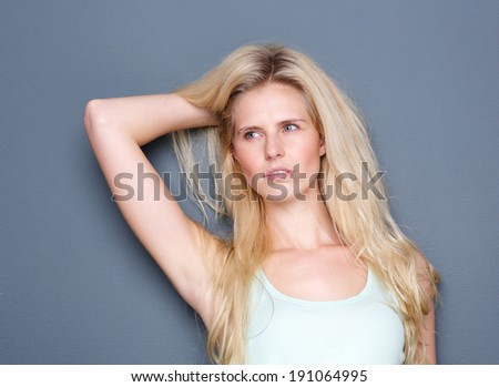 Close up portrait of a sensual young blond woman posing with hand in hair on gray background