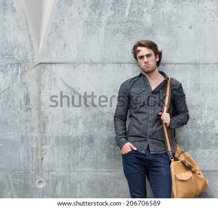 Portrait of a stylish young man posing with travel bag outdoors