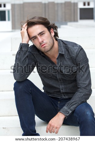 Close up portrait of a cool guy sitting outside with hand in hair