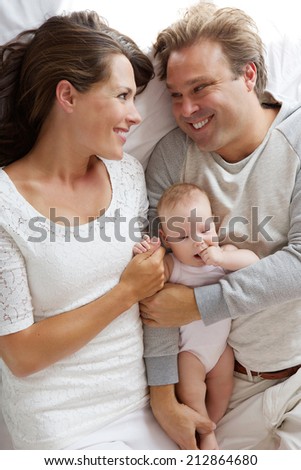 Close up portrait of a smiling man and woman hugging baby in bed