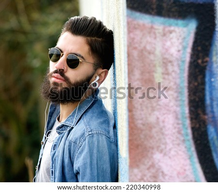 Close up portrait of a modern young man with beard listening to music with earphones