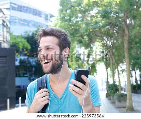 Close up portrait of a handsome young man smiling with mobile phone and earphones